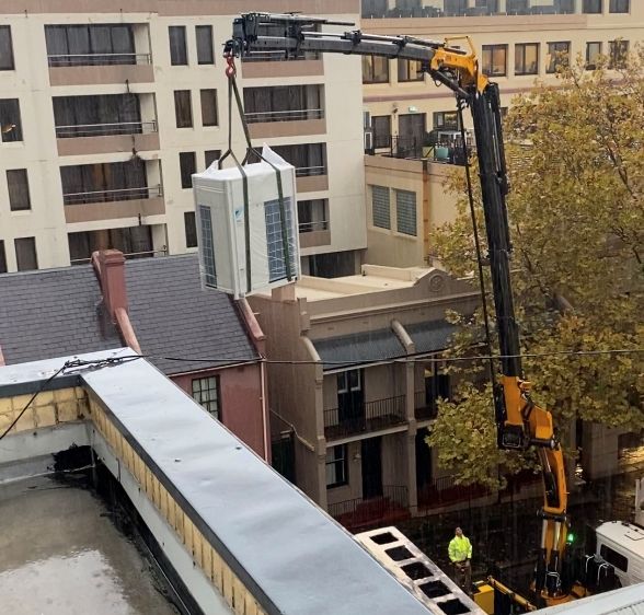 Crane lifting a large HVAC unit amidst Sydney's urban buildings, exemplifying Mechair Engineering Solutions' expertise and commitment to excellence in construction and building services